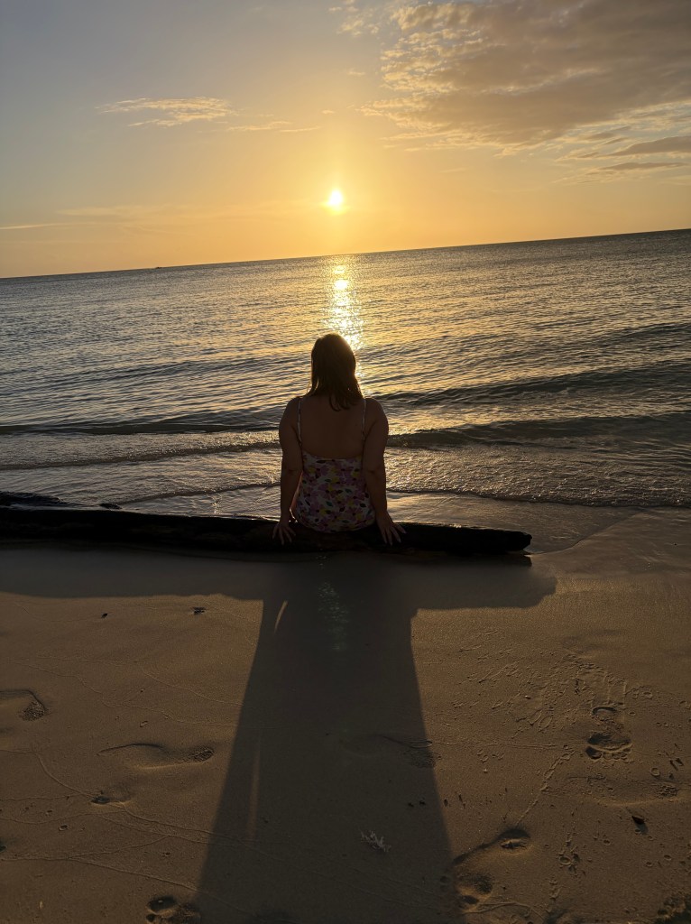 Jenniffer sitting by the ocean watching the sunset.